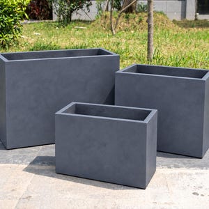 May include: A set of three rectangular planters in a dark grey finish. The planters are arranged in a tiered formation, featuring clean lines and a smooth, solid construction with open tops for planting various greenery or flowers.