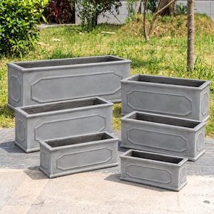 May include: A set of six rectangular grey planters of varying sizes, each featuring a raised octagonal panel design on the front and sides. These containers have a smooth, matte finish and an open top, arranged in a tiered formation on a paved surface.