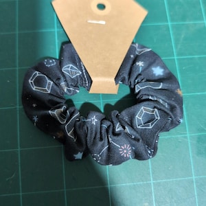 May include: A black scrunchie with a white and blue geometric pattern. The scrunchie is made of fabric and has a gathered design.