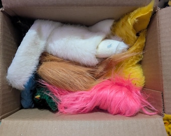 May include: A cardboard box containing assorted faux fur pieces in a variety of colours. The fur includes white, pink, yellow, and brown. The pieces are likely for a costume or craft project.