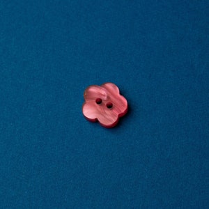 May include: A pink plastic button with a flower shape and two holes in the center.