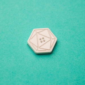 May include: White button with a geometric design and four small dots in the center.