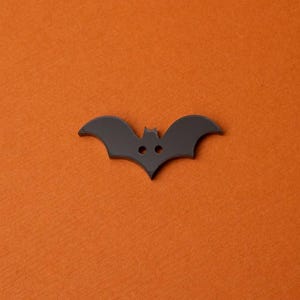 May include: Black bat-shaped button with two small white circles for eyes.