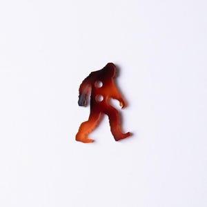 May include: A brown and orange Bigfoot silhouette button.