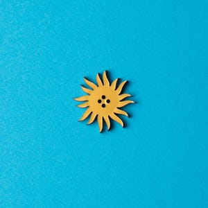 May include: A yellow wooden sun-shaped button with four holes in the center.