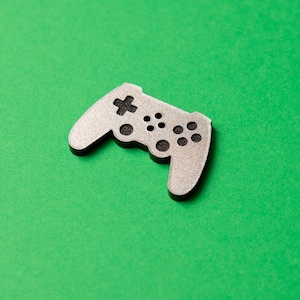 May include: A silver-colored plastic game controller with black buttons, on a green background.