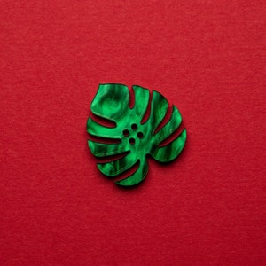 May include: A green monstera leaf shaped button with a marbled pattern.