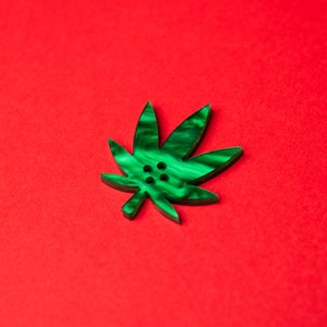 May include: A green leaf-shaped button with four holes in the center. The button is on a red background.