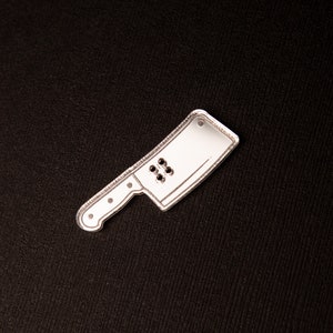 May include: A silver metal cutout of a chef's knife with a rounded tip and a handle with four holes.
