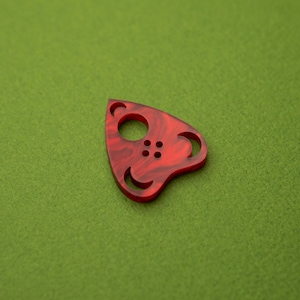 Pode incluir: Um pingente vermelho em forma de triângulo com um círculo e um design de lua crescente. O pingente é feito de resina e tem um efeito marmorizado.