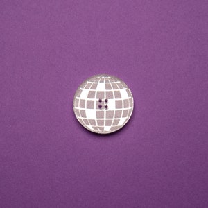 May include: A white and gray button with a globe design. The button has four holes in the center.