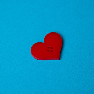 May include: A red heart-shaped button with four holes in the center, against a bright blue background.
