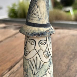 May include: A hand-carved, off-white and blue wizard figurine with a pointed hat. The hat features a carved geometric design. The wizard has a long white beard and is holding a bird. The figurine is approximately 15 cm tall.