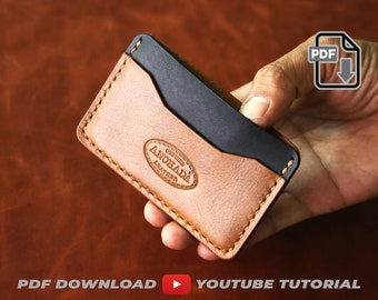 May include: A brown leather card holder with a black leather interior and a stitched edge. The card holder has the text "GENUINE ANOHA DA LEATHER" embossed on the front.