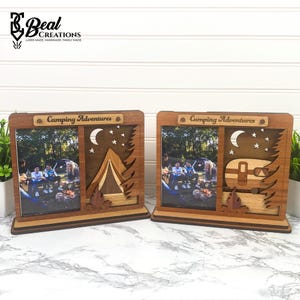 May include: Two wooden photo frames with camping-themed designs. One frame features a tent, moon, and stars, while the other showcases a camper. Both frames have the text "Camping Adventures" and are made of layered wood.