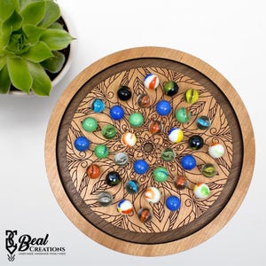May include: A wooden marble run game with a mandala design. The game is made of cherry wood and has a walnut inlay. The game comes with 25 marbles in various colors, including blue, green, red, orange, and white.