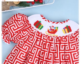 Peut inclure: Robe à motifs rouges et blancs avec un col blanc orné de cadeaux de Noël brodés et du Père Noël dans un traîneau. La robe a des manches courtes bouffantes et le texte "High Cotton Magnolias" dans le coin supérieur gauche.