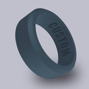 May include: A dark teal silicone ring with the word "CUSTOM" embossed on the side. The ring is a solid color and has a smooth, rounded design. The ring is approximately 0.3 inches wide.