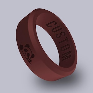 May include: A maroon silicone ring with the word "CUSTOM" engraved on the outside. A small panda bear graphic is on the side of the ring. The ring is a solid color and has a smooth texture.