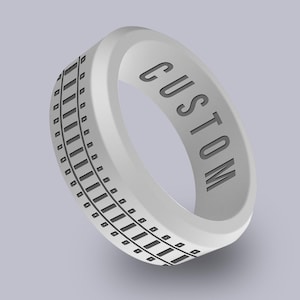 May include: A white silicone ring with a black railroad track design and the word "CUSTOM" engraved on the side.