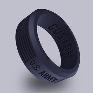 May include: A navy blue silicone ring with the text "CUSTOM" and "U.S. ARMY" embossed on the band. The ring features a textured American flag design. A military-themed accessory.
