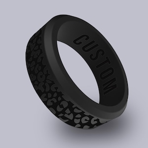 May include: Black silicone ring with a leopard print pattern on the outer band. The word "CUSTOM" is embossed on the inner band. The ring is a solid black color.