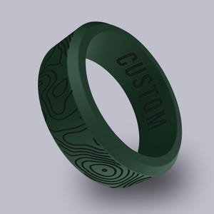 May include: Dark green silicone ring with a topographic map design and the word "CUSTOM" engraved on the band. The ring is a solid color with a matte finish, and the design is a darker shade of green.