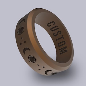 May include: A tan silicone ring with the word "CUSTOM" engraved on the side. The ring features a celestial design with suns, moons, and stars. The ring is a unique piece of jewelry.