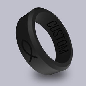 May include: A black silicone ring with the word "CUSTOM" engraved on the side and a fish symbol engraved on the other side.
