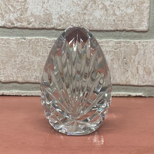 May include: A clear glass paperweight in the shape of an egg with a cut-glass design.