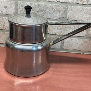 May include: A silver aluminum coffee pot with a black knob on the lid. The pot has a long handle and a round body.