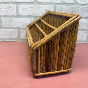 May include: Angled bamboo desk organizer with three compartments. The organizer is made of natural-colored bamboo and has a warm, rustic appearance. The compartments are separated by vertical dividers, and the piece sits on a flat base.