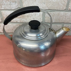 May include: A silver aluminum tea kettle with a black handle and a black knob on the lid.