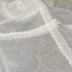 May include: White sheer fabric with a delicate lace trim. The fabric has a slight crinkle texture and a few brown stains.