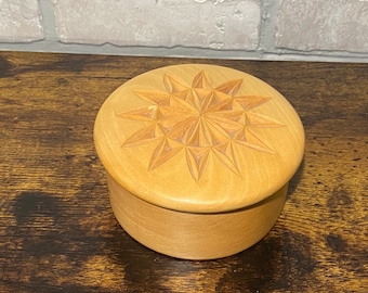 May include: A small, round wooden box with a carved starburst design on the lid. The box is made of light wood and has a natural finish.