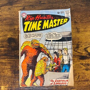 May include: A vintage comic book cover featuring Rip Hunter, Time Master. The cover art depicts a large, orange, reptilian creature with a scaly, yellow shell. The text on the cover reads "Rip Hunter... Time Master" and "The Earthling of 5,000,000!"