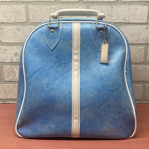 May include: A blue vintage travel bag with white trim and a white stripe down the center. The bag has a white zipper and a metal tag with the word "La Paz" on it.