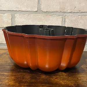 May include: A red and black bundt cake pan with a fluted design. The pan is made of metal and has a non-stick coating.
