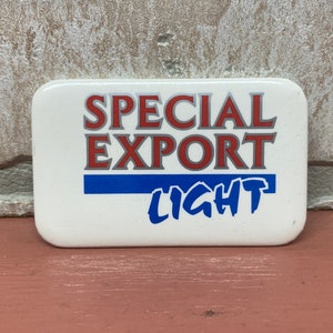 May include: A white button with the text "SPECIAL EXPORT LIGHT" in red, blue, and gray lettering.