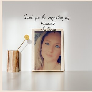 Pu&ograve; includere: Una foto incorniciata di una donna con capelli biondi e occhi azzurri. La foto &egrave; su una superficie bianca con un piccolo vaso con un fiore giallo. Il testo "Thank you for supporting my business! -Brittney" &egrave; sopra la foto.