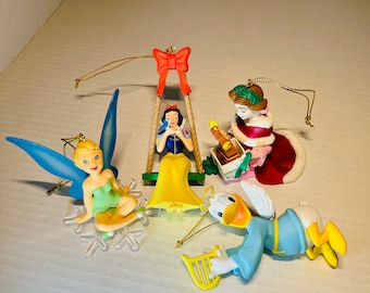 Pode incluir: Conjunto de cinco enfeites de Natal vintage da Disney com Branca de Neve em um balanço, Sininho em um floco de neve, uma menina com um vestido vermelho e Donald Duck tocando harpa. Os enfeites são feitos de plástico e têm um cordão dourado para pendurar.