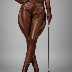 May include: A brown leather riding outfit, including a fitted shirt, jodhpurs, gloves, belt, and boots. The outfit is paired with a riding crop. The clothing is a rich brown color, and the background is a solid gray.