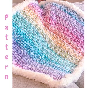 May include: A rainbow crochet baby blanket with a white faux fur border. The blanket is made with a textured stitch and has a soft, fluffy feel.