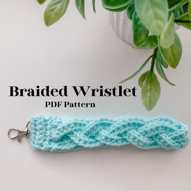 May include: A light blue braided wristlet with a silver key chain. The wristlet is made of yarn and has a braided design. The text "Braided Wristlet PDF Pattern" is written in black text on a white background.