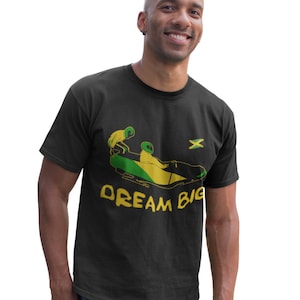 May include: Black t-shirt with a green and yellow graphic of two people riding a Jamaican flag-themed bobsled. The text "DREAM BIG" is printed below the graphic.