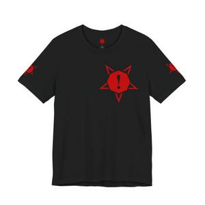 Può includere: Una t-shirt nera a maniche corte con una grafica rossa sul petto e su entrambe le maniche. La grafica consiste in una stella a cinque punte che circonda un ottagono rosso con un punto esclamativo nero al centro. Un piccolo logo è sul collo.