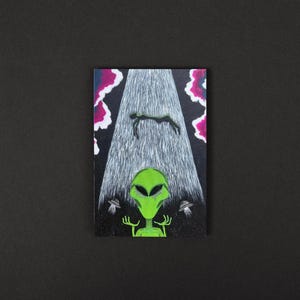 May include: A green alien with large eyes and a black background. The alien is holding up its hands, and there are two small flying saucers above its head. A person is being abducted by a beam of light from the sky.