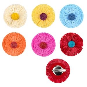 May include: A selection of colourful, circular flower-shaped brooches. The brooches are made of layered, fringed paper in various colours, including yellow, orange, pink, red, and blue. Each brooch has a contrasting centre and a pin backing.