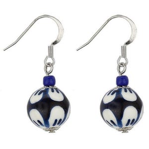 Puede incluir: Un par de pendientes colgantes con cuentas estampadas en azul oscuro y blanco. Las cuentas tienen forma redonda con un diseño floral blanco. Los pendientes tienen ganchos plateados y una pequeña cuenta azul encima de la cuenta estampada.