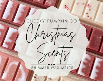 May include: A collection of rectangular wax melts in shades of red, pink, and cream, some featuring white swirls or small red star and peppermint-shaped sprinkles. A central label reads CHEEKY PUMPKIN CO Christmas Scents SHIMMER WAX MELTS.
